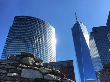 Irish Hunger Memorial stone wall in front of modern Manhattan skyscrapers under a clear blue sky.