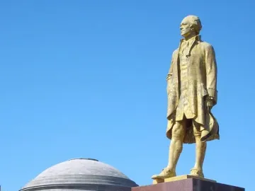 Alexander Hamilton statue on a stone pedestal with a domed classical building in the background