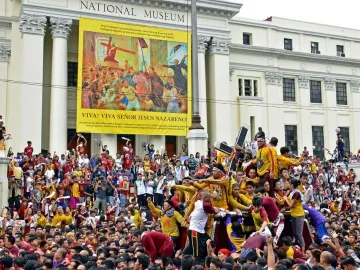 The Black Nazarene statue is carried on a platform through a dense crowd, with people reaching out toward it.