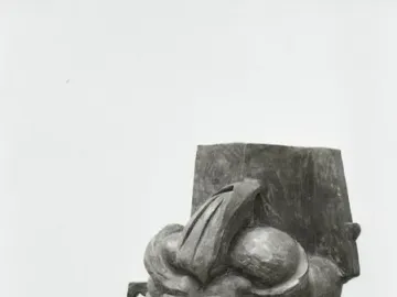 L\'antigrazioso bust with fragmented, distorted facial features on a dark slatted base.