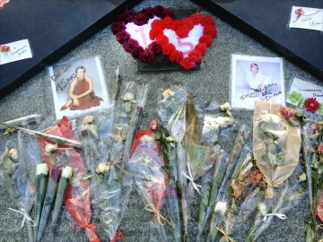 A memorial on a dark granite surface with wrapped bouquets, two framed photos of Princess Diana, and a heart-shaped floral wreath marked 15.