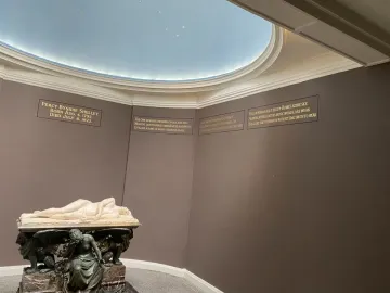Shelley Memorial with a white marble reclining male figure on a sarcophagus, supported by a seated bronze figure.