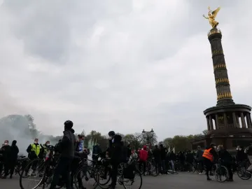 Victory Column in Berlin with a crowd of cyclists gathered around its base under a cloudy sky.