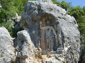 Athena relief carved into a rock face, with a robed figure, a standing column, and carved inscriptions beside it.