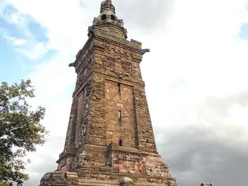 The Kyffhäuser Monument’s Barbarossa Tower rises in reddish-brown stone above a paved forecourt with benches and planting beds.