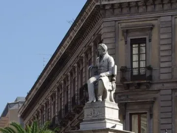 Monument to Vincenzo Bellini with a seated figure atop a marble pedestal and allegorical statues below.