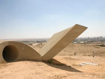 Monument to the Negev Brigade, a large abstract concrete sculpture on a sandy hillside with a city in the distance.