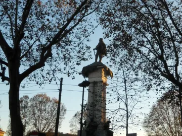 Monument to Vittorio Emanuele II seen from below, with a statue atop an ornate column against a blue sky.