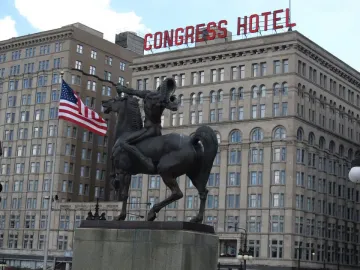 The Bowman and The Spearman bronze equestrian statue on a stone pedestal with a Congress Hotel sign and American flag in the background.