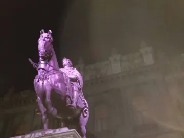 El Caballito equestrian statue lit in purple at night on a tall stone pedestal, with an ornate building behind it.