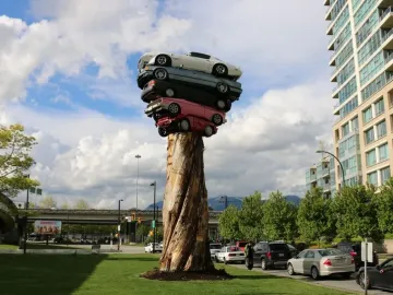 Trans Am Rapture sculpture with five cars stacked on a tall wooden column in a grassy urban setting