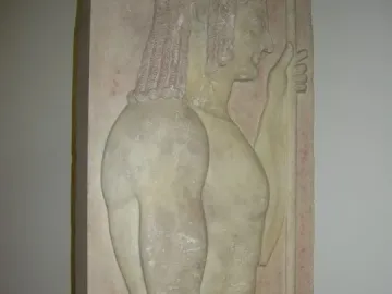 Grave stele with a carved male figure in profile facing right, holding a staff and showing traces of red pigment.