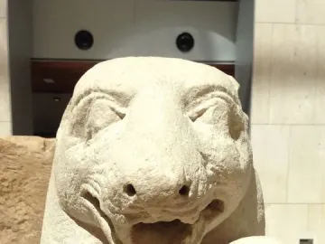 Close-up of the Bear of Porcuna showing a carved animal head and upper torso with an open mouth and closed eyes, with a smaller human head beside it.