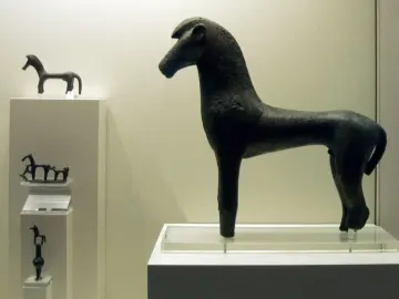 A dark bronze horse figure stands on a pedestal in a museum display.