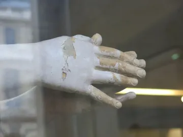 Clasped hands from the Mary Magdalene penitente sculpture, with peeling light-colored surface exposing darker material underneath.