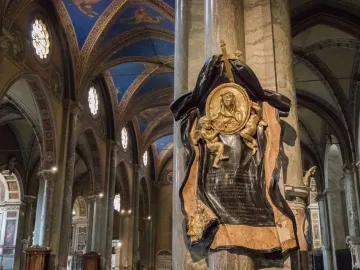 The Memorial to Maria Raggi shows a gilded medallion with a female figure and cherubs mounted on a marble column inside a grand church interior.