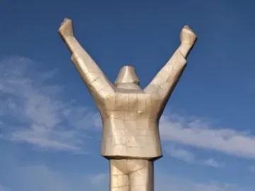 Monument to Stjepan Filipović, a silver-toned faceted statue with raised clenched fists on a graffiti-marked base against the sky.