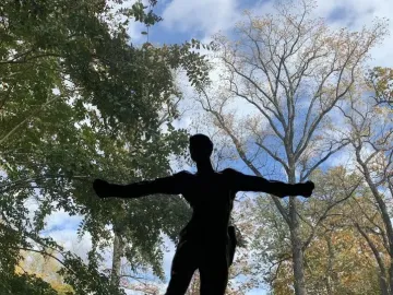 Standing Mercury by Auguste Rodin silhouetted against a bright blue sky with trees behind it.