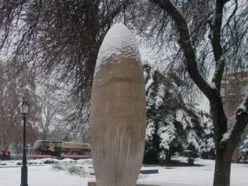 Zero Kilometre Stone topped with snow in a snowy park, with bare trees in the background.