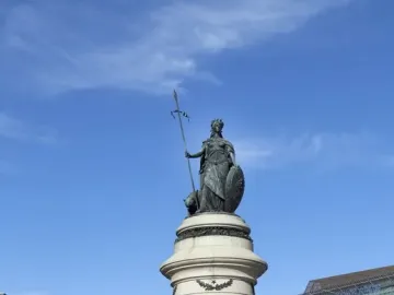 Pioneer Monument in San Francisco, with a bronze crowned female figure atop a tall stone column, sculptural groups at the base, and a fenced foreground.