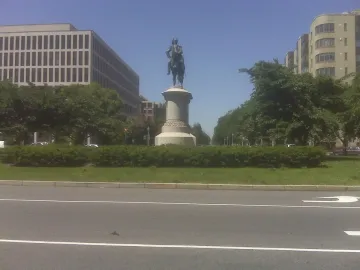Winfield Scott equestrian statue on a tall pedestal in a grassy median with trees and city buildings behind it.