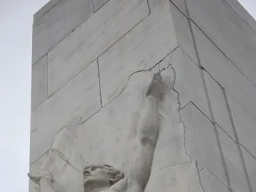 Close-up of the Alamo Cenotaph showing a stone relief of a muscular man with raised arms.