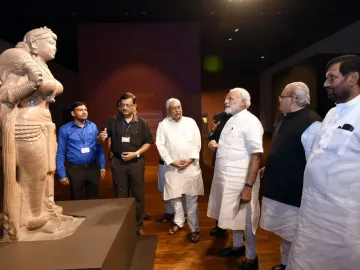 Didarganj Yakshi statue displayed on a dark pedestal in a museum, with part of the left arm missing and visitors standing nearby.