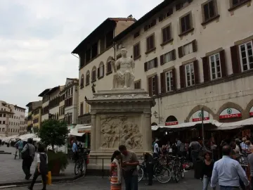 Giovanni delle Bande Nere statue on an ornate pedestal in a busy square with bicycles and pedestrians nearby.