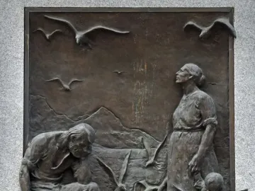 Bronze relief on the Seagull Monument showing a kneeling man and standing woman surrounded by seagulls, with mountains in the background.