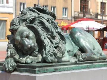 Sleeping Lion bronze sculpture with a green patina, shown lying with its head resting on its front paws.