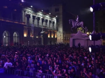 El Caballito equestrian statue lit with purple stage lights at night, with a crowd and event tents in front of it.