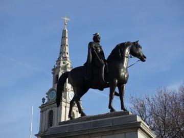 Equestrian statue of George IV on a stone pedestal, with a church steeple and clock tower behind it.