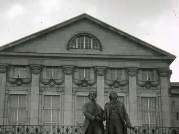 Goethe and Schiller Monument on a pedestal in front of a classical building, with people gathered in the square.