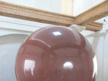 Large Red Sphere on a dark stepped pedestal in a bright room with wooden beams overhead.