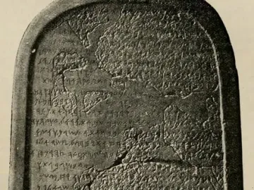 The Mesha Stele, a dark ancient stone slab with a rounded top covered in carved inscriptions and visible cracks.