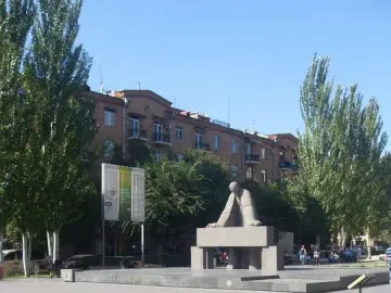 Monument to Alexander Tamanyan on a paved plaza with trees, buildings, and a stone fountain nearby.