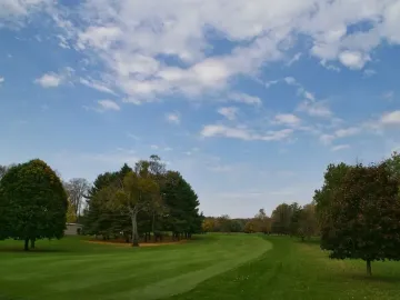 Grassy landscape at Newark Earthworks with mowed stripes and trees along the edges under a partly cloudy sky.