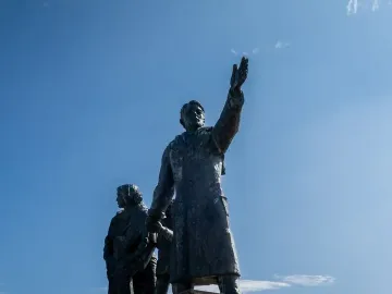 Auswandererdenkmal sculpture with a figure waving from a group of dark metal figures on a tall stone pedestal.