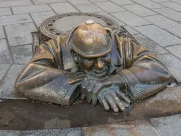 Čumil bronze statue of a man emerging from a manhole in a stone-paved street