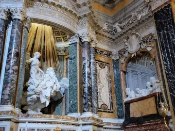 Ecstasy of Saint Teresa marble sculpture with an angel above a reclining figure under golden rays in an ornate niche.