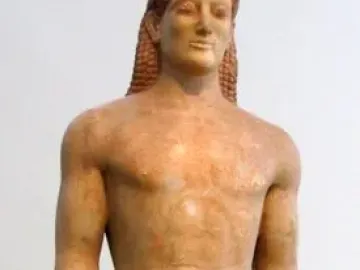 Kroisos Kouros, a front-facing ancient marble statue of a nude young man with braided hair, standing with one leg forward.