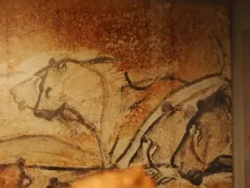 Blurred Lion-man sculpture in the foreground with cave-painting-style animal figures on the wall behind it.