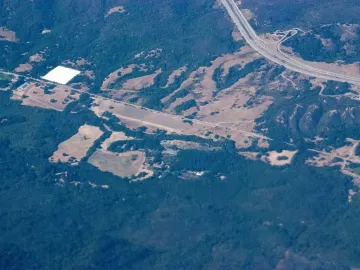 Aerial view of the Pulgas Water Temple surrounded by forest and open land near a highway.