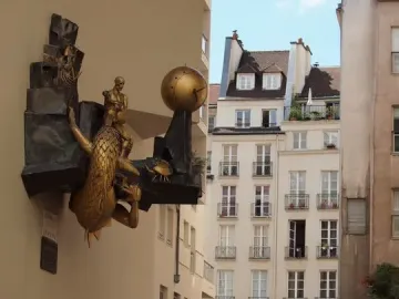 The Defender of Time sculpture with a bronze dragon-like creature, seated figure, and gold clock orb on a building facade.