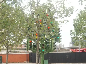 Traffic Light Tree sculpture glowing with red, yellow, and green lights among surrounding trees in an urban setting.