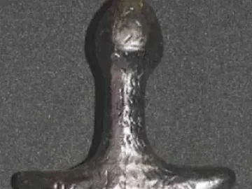 Back view of the Venus of Langenzersdorf sculpture, a dark stylized female figurine with broad shoulders and rounded hips.