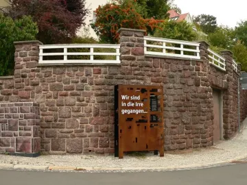 Dejudaization Institute memorial sign beside a curved stone wall and sidewalk in Eisenach.