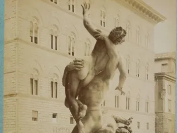 Giambologna’s Rape of the Sabine Women sculpture in a public square, with three intertwined figures against a building with arched windows.