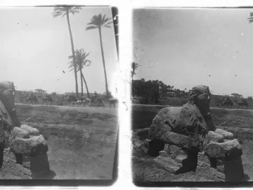 A weathered sphinx of Memphis stands in a desert landscape with palm trees and camel riders in the distance.