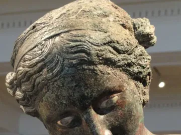 Close-up of The Cleveland Apollo’s bronze head with a greenish-brown patina and downward gaze.